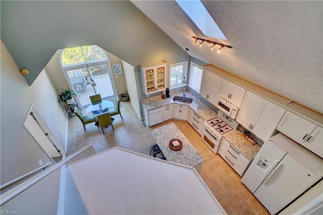 kitchen with white cabinetry, a wealth of natural light, vaulted ceiling with skylight, and white appliances