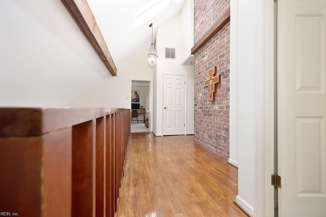 hallway with beam ceiling, wood-type flooring, high vaulted ceiling, and brick wall