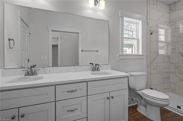 bathroom with hardwood / wood-style flooring, vanity, toilet, and a tile shower