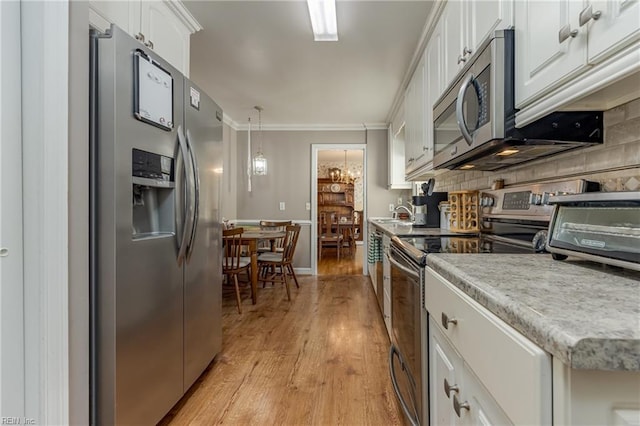 kitchen featuring pendant lighting, light hardwood / wood-style flooring, appliances with stainless steel finishes, white cabinets, and decorative backsplash