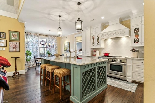 kitchen with pendant lighting, white cabinets, a center island with sink, custom exhaust hood, and range with two ovens