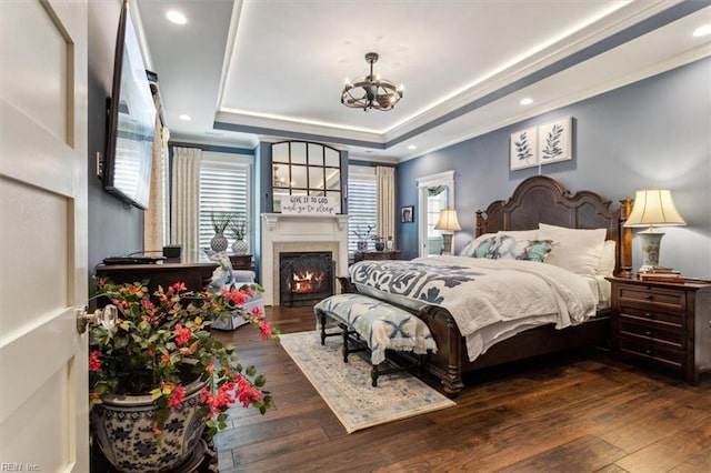 bedroom featuring dark wood-type flooring, ornamental molding, a tray ceiling, and a chandelier