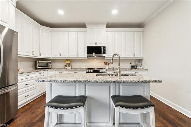 kitchen with an island with sink, appliances with stainless steel finishes, sink, and white cabinets