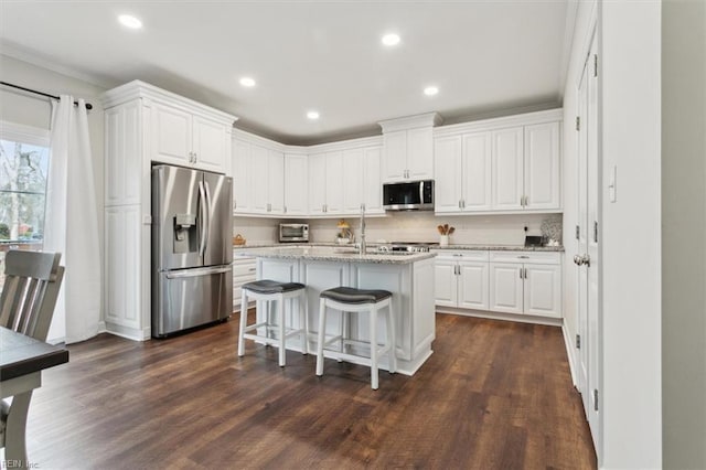 kitchen with white cabinetry, a kitchen breakfast bar, an island with sink, stainless steel appliances, and light stone countertops