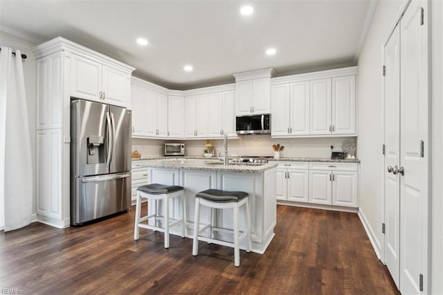 kitchen with appliances with stainless steel finishes, a kitchen island with sink, light stone countertops, white cabinets, and dark hardwood / wood-style flooring