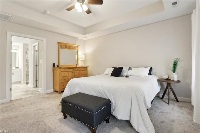 bedroom featuring connected bathroom, light carpet, ceiling fan, and a tray ceiling