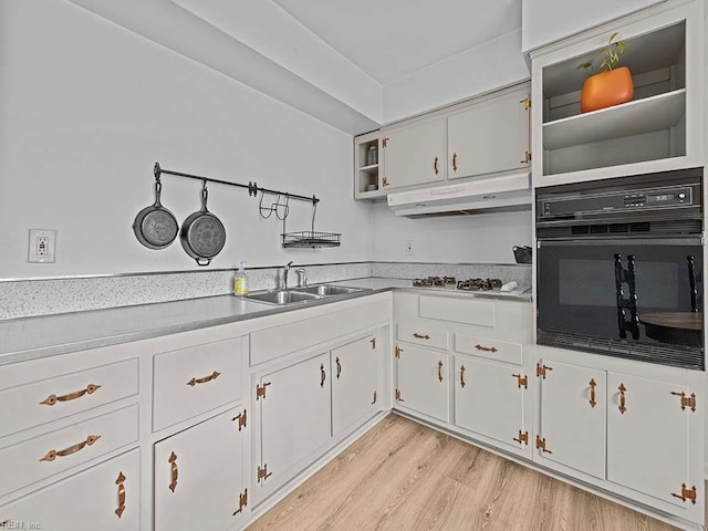 kitchen with black oven, sink, light hardwood / wood-style flooring, white cabinets, and white gas cooktop