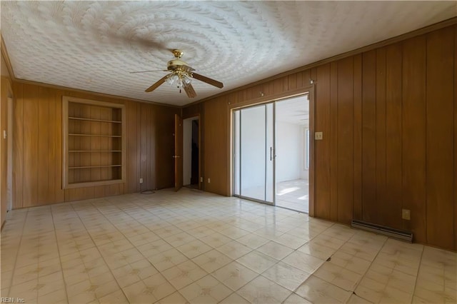 empty room with built in features, wooden walls, ornamental molding, ceiling fan, and baseboard heating