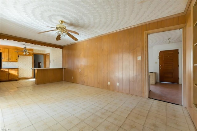 unfurnished living room featuring ornamental molding, ceiling fan, and wood walls