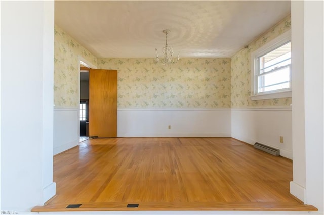 spare room with hardwood / wood-style floors, a chandelier, and baseboard heating