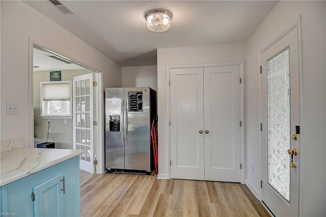 kitchen featuring stainless steel fridge, visible vents, blue cabinets, light stone countertops, and light wood-type flooring