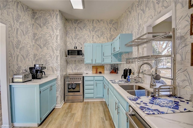 kitchen featuring a sink, light countertops, blue cabinetry, appliances with stainless steel finishes, and wallpapered walls