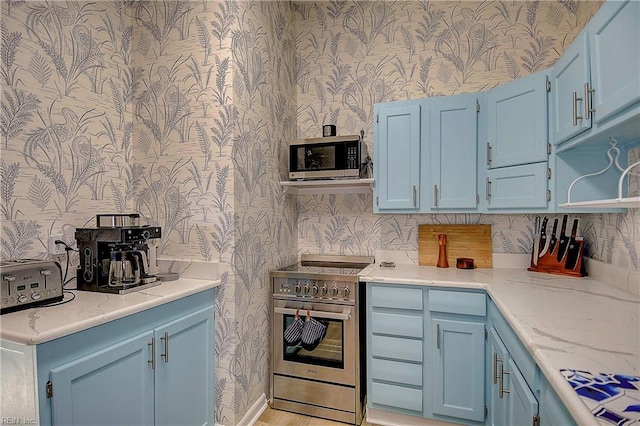 kitchen with blue cabinetry, appliances with stainless steel finishes, and wallpapered walls