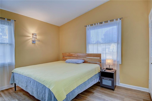 bedroom with vaulted ceiling, wood finished floors, and baseboards