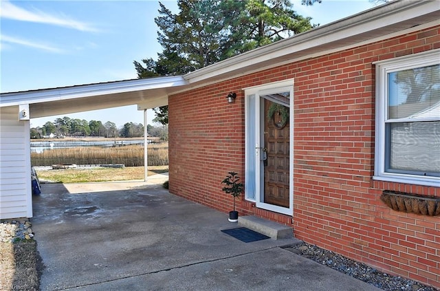 view of exterior entry featuring a carport, brick siding, and driveway