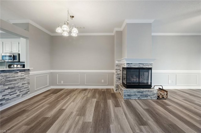 unfurnished living room with crown molding, a notable chandelier, a fireplace, and light wood-type flooring