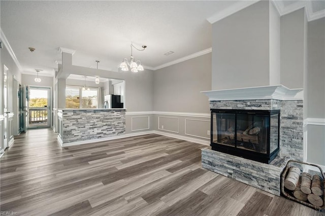 unfurnished living room featuring hardwood / wood-style flooring, ornamental molding, a fireplace, and a notable chandelier