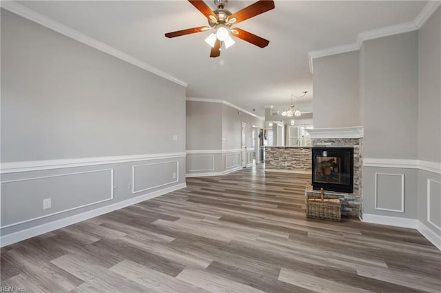 unfurnished living room featuring hardwood / wood-style flooring, ceiling fan with notable chandelier, ornamental molding, and a stone fireplace