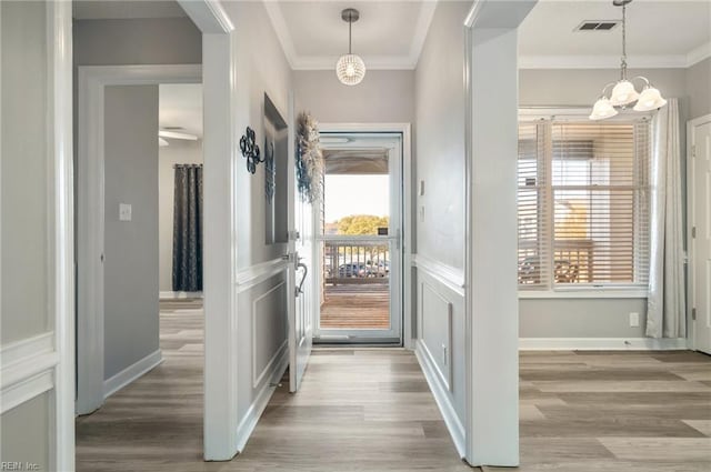 corridor with ornamental molding, a chandelier, and light wood-type flooring