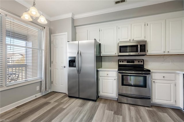 kitchen with appliances with stainless steel finishes, pendant lighting, white cabinetry, ornamental molding, and light hardwood / wood-style floors