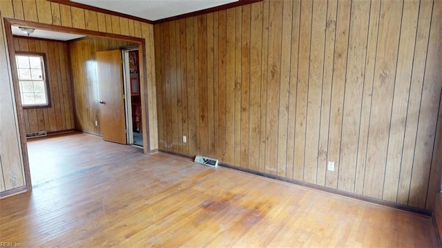 spare room with light wood finished floors, visible vents, crown molding, and wood walls