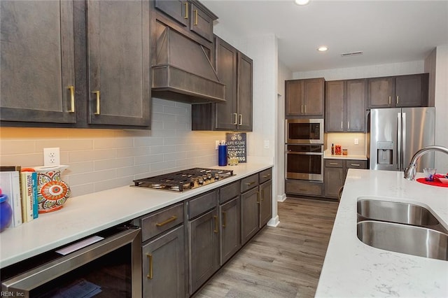 kitchen featuring sink, light wood-type flooring, custom range hood, stainless steel appliances, and beverage cooler