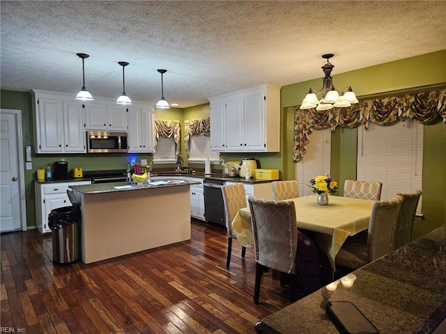 kitchen with white cabinetry, decorative light fixtures, a kitchen island, dark wood-type flooring, and appliances with stainless steel finishes