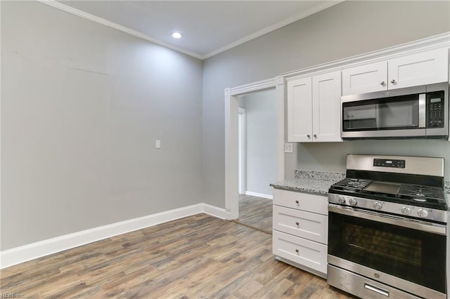 kitchen featuring white cabinetry, crown molding, hardwood / wood-style flooring, stainless steel appliances, and light stone countertops