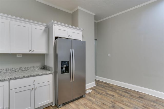 kitchen featuring white cabinetry, crown molding, stainless steel fridge, and light stone countertops