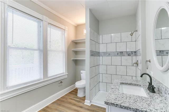 bathroom with a tile shower, hardwood / wood-style flooring, vanity, ornamental molding, and toilet