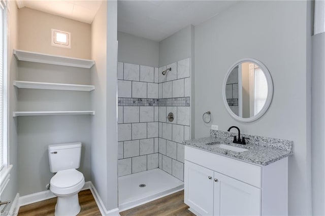 bathroom with wood-type flooring, tiled shower, vanity, and toilet