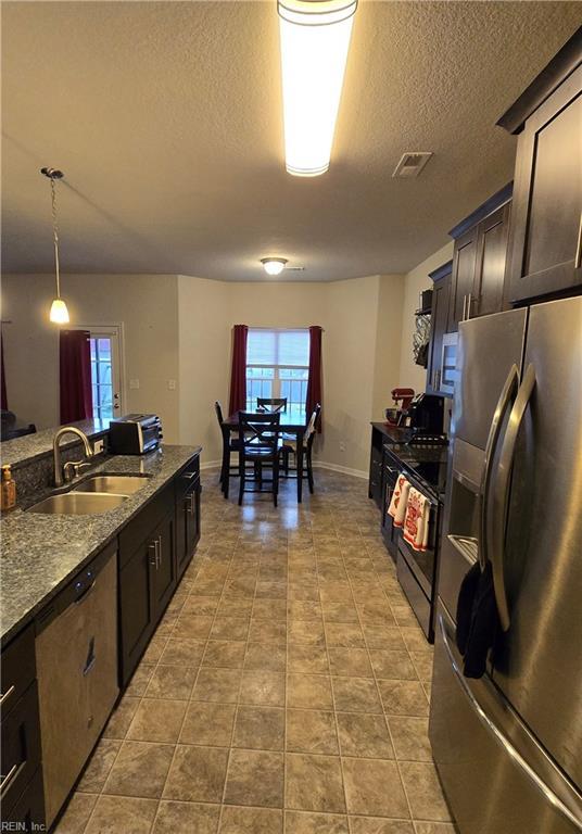 kitchen with dark brown cabinetry, sink, light stone counters, pendant lighting, and stainless steel appliances