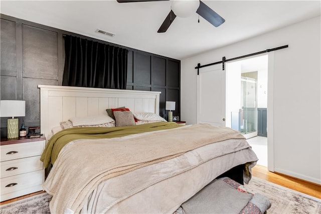 bedroom with ceiling fan, a barn door, light wood-type flooring, and ensuite bath