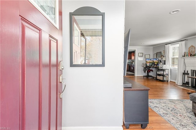 foyer entrance featuring a brick fireplace, ornamental molding, and light wood-type flooring