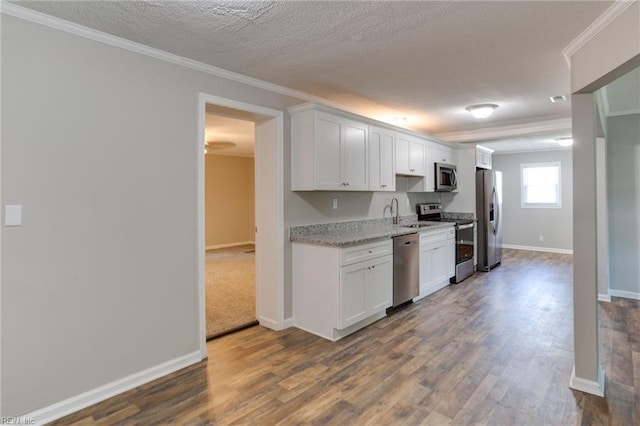 kitchen with ornamental molding, appliances with stainless steel finishes, dark hardwood / wood-style floors, and white cabinets