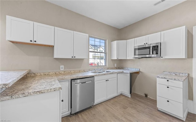 kitchen with stainless steel appliances, white cabinetry, sink, and light hardwood / wood-style flooring