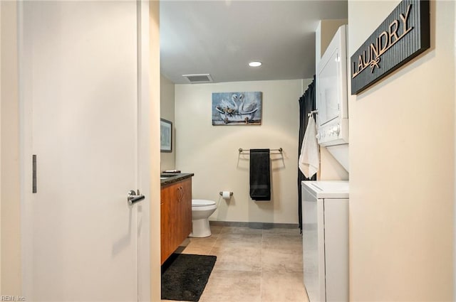 bathroom featuring tile patterned flooring, vanity, stacked washer and clothes dryer, and toilet