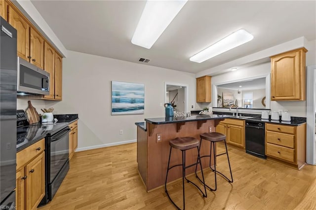 kitchen featuring a kitchen island, light wood-type flooring, a kitchen bar, and black appliances