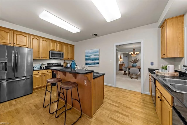 kitchen with sink, a breakfast bar area, a center island, black appliances, and light wood-type flooring