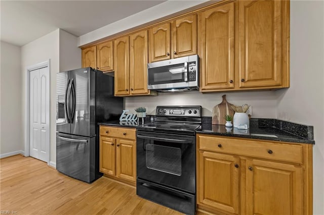 kitchen with dark stone countertops, light wood-type flooring, and black appliances