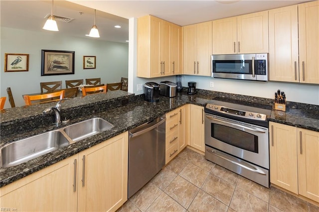 kitchen featuring appliances with stainless steel finishes, light brown cabinets, and decorative light fixtures