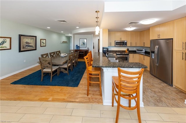 kitchen with a kitchen bar, sink, decorative light fixtures, light brown cabinets, and appliances with stainless steel finishes