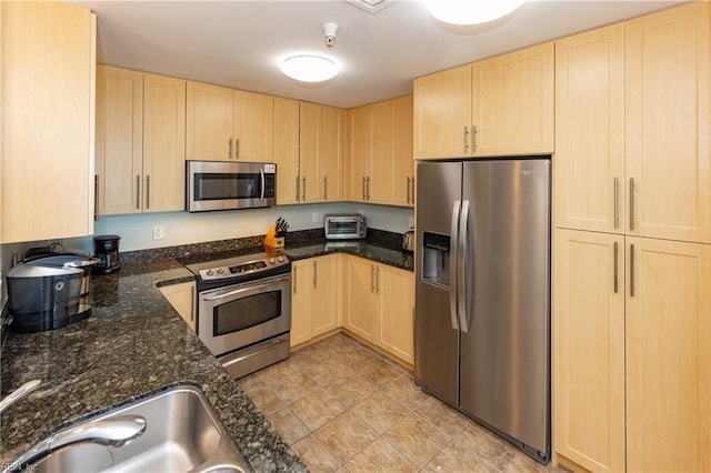 kitchen with dark stone countertops, appliances with stainless steel finishes, and light brown cabinets