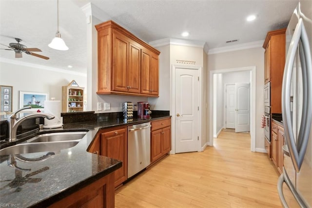 kitchen featuring appliances with stainless steel finishes, light wood-type flooring, crown molding, sink, and dark stone countertops