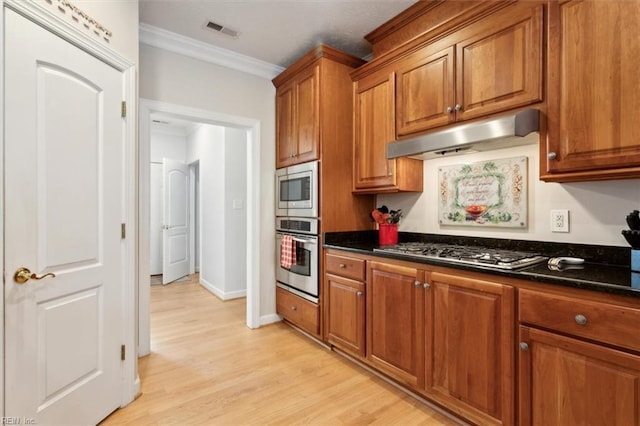 kitchen featuring crown molding, stainless steel appliances, dark stone counters, and light wood-type flooring