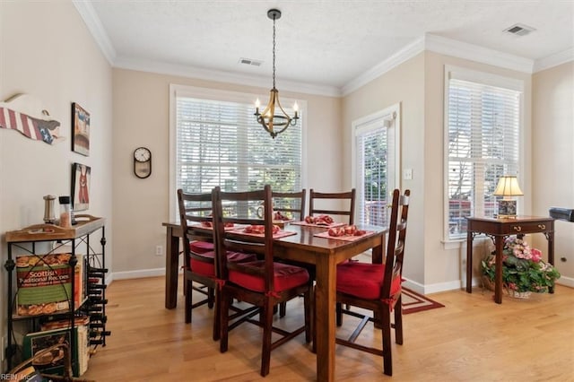 dining room with light wood-type flooring, ornamental molding, and an inviting chandelier