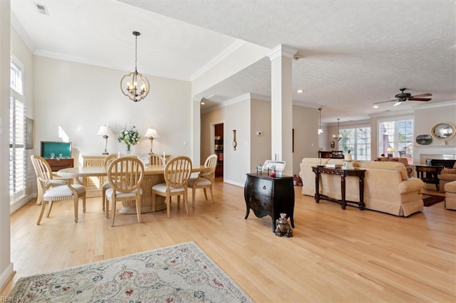 dining area featuring light wood-type flooring, ornate columns, crown molding, and a textured ceiling