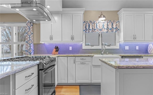 kitchen featuring island exhaust hood, light stone countertops, white cabinets, and stainless steel gas stove