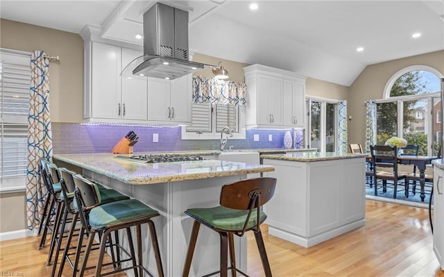 kitchen featuring a breakfast bar area, light stone counters, island range hood, a kitchen island, and white cabinets