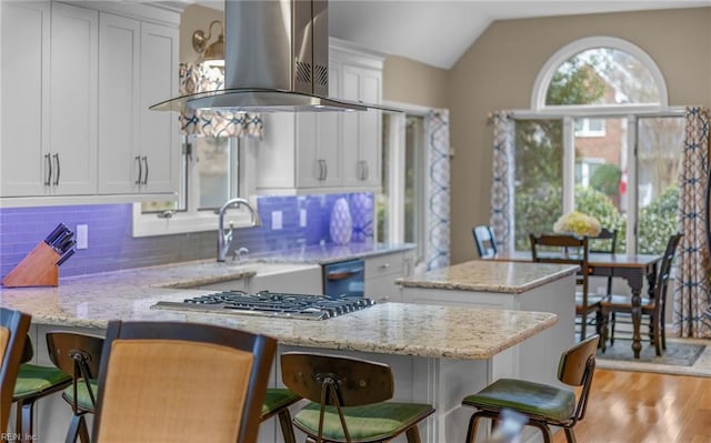 kitchen with a kitchen breakfast bar, light stone counters, island range hood, a kitchen island, and vaulted ceiling